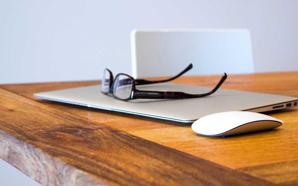 A desk with a laptop, spectacles and a few notes
